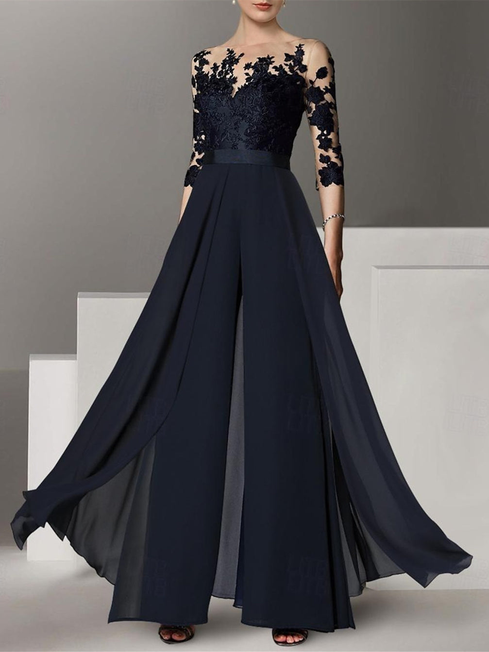 A black chiffon A-line/princess silhouette cocktail pantsuit with a jewel neckline, 3/4 length sleeves, and applique embellishments.